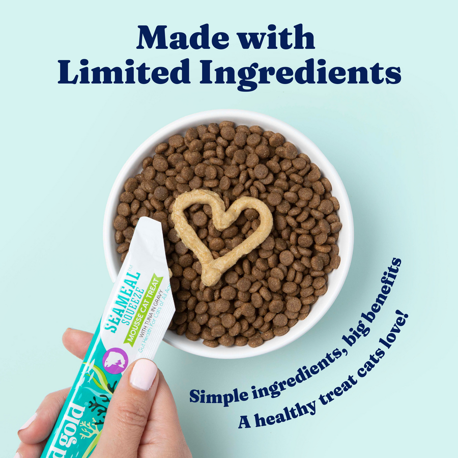 Bowl of cat kibble with a heart shape made from mousse treat, and a hand holding a squeeze packet.
