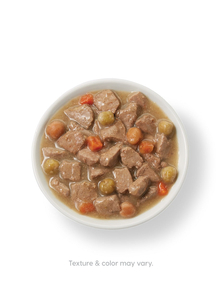 Wet dog food in a bowl featuring chunks of turkey, carrots, and peas in a gravy-like sauce.